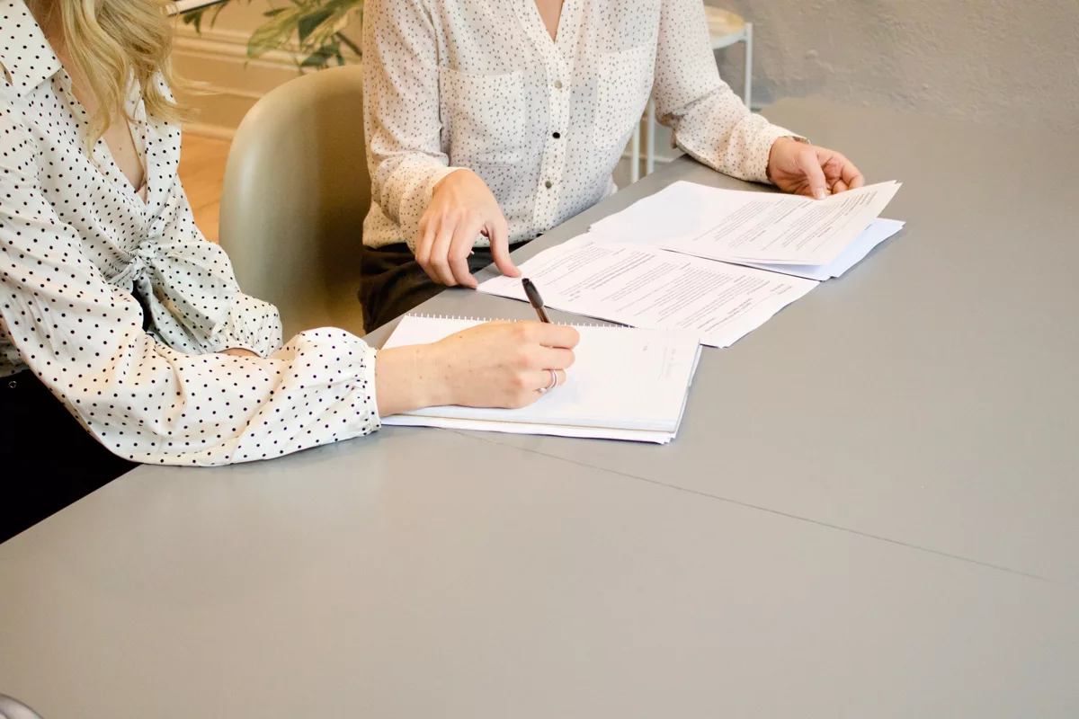 woman signing on white printer paper beside woman about to touch the documents.jpg