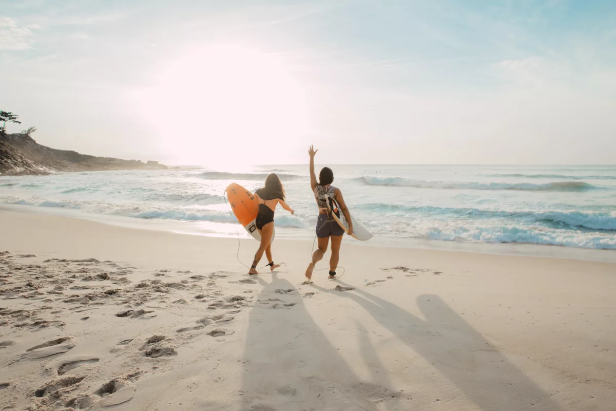 two women walking towards the ocean carrying surfboards during day.jpg